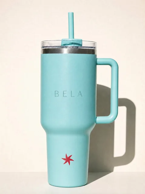 Termo turquesa con el nombre de Bela y el spark rojo, con flash directo sobre fondo crema